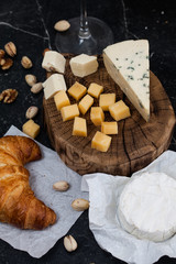 Tasting cheese dish on a wooden plate. Cheese assorted - blue cheese, camembert, cheddar and parmesan. Food for wine and romantic, cheese delicatessen on a black marble table. Top view with copy space