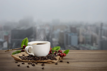 Hot coffee cup with fresh organic red coffee beans and coffee roasts on the wooden table and the city background