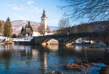 Obraz premium winter view of gothic church and stone bridge in ribcev laz, lake bhoinj, slovenia.