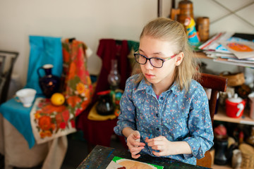 Fototapeta premium Portrait of blonde girl with big black glasses smiling happily while enjoying art and craft lesson in art school working together with other kids