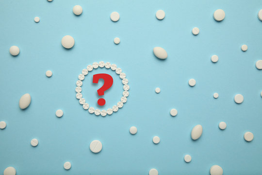 White pills for pain relief and treatment on a blue background. Question mark, the choice of drugs.
