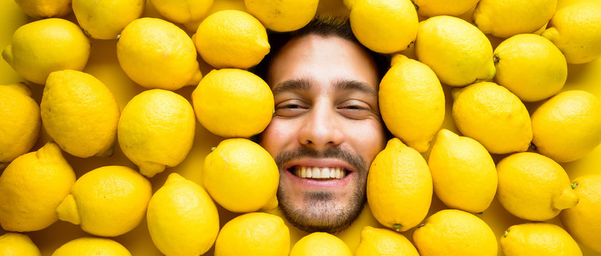 Mann mit Zitronen, Konzept für die Lebensmittelindustrie. Gesicht des lachenden Mannes in der Zitronenoberfläche.