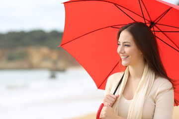 Happy woman looks at side holding red umbrella on the beach