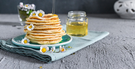 Many small pancakes with honey or syrup. Delicious traditional breakfast. Spring flowers as food styling in photography. Gray stone background and dessert is sweet. Free space for the test.