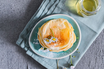Many small pancakes with honey or syrup. Delicious traditional breakfast. Spring flowers as food styling in photography. Gray stone background and dessert is sweet. Free space for the test.