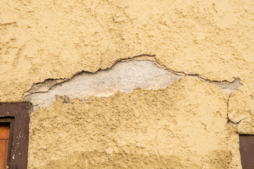 Obraz premium yellow plaster on a house wall which has a crack and crumbles off as a background