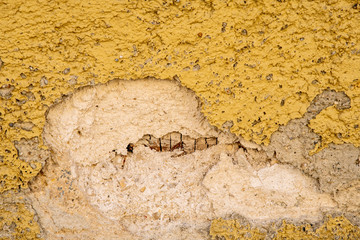 yellow plaster on a house wall which has a crack and crumbles off as a background