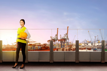 Pretty asian female worker with safety vest holding the hard hat standing on office terrace