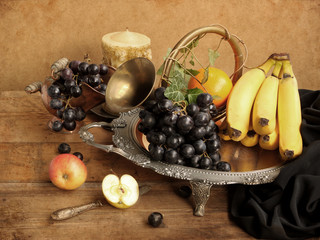 Grapes, bananas, apples and oranges on a beautiful metal dish with black drapery fabric, cornucopia