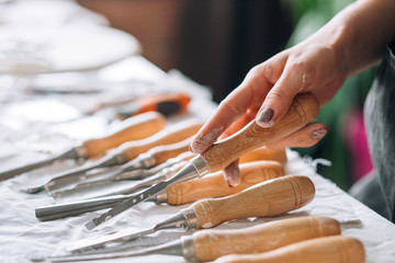 Fototapeta na wymiar Carving tools assortment. Craft set composition arranged on table. Woman hand choosing chisel.