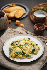 Scrambled eggs with spinach, cup of tea on dark brown background. Vertical. Breakfast with Pan-fried omelette, side view, close up