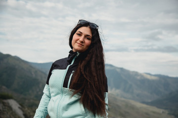 Naklejka premium Girl smiling in a turquoise jacket sitting on the mountain. Enjoys the beautiful view around.