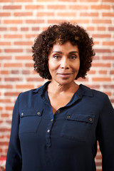 Portrait Of Smiling Mature Businesswoman Standing Against Brick Wall In Modern Office