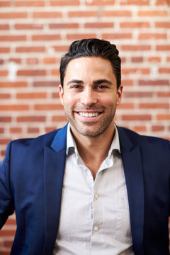 Portrait Of Smiling Mature Businessman Standing Against Brick Wall In Modern Office