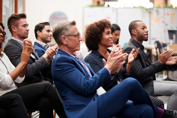 Group Of Businessmen And Businesswomen Applauding Presentation At Conference
