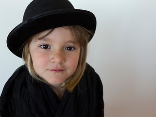 Cute serious looking little girl wearing a black bowler hat and shawl