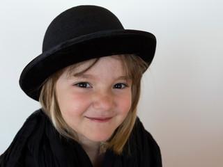 Closeup of cute smiling little girl wearing a black bowler hat and shawl