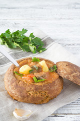 Traditional Hungarian Goulash soup with parsley and green onions in a bread on a white and brown rustic background with copy space