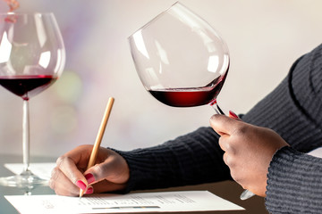 African female sommelier evaluating red wine at table.