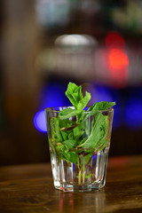 Fresh mojito isolated on blurred background. The leaves of green mint in the glass with water on wooden table. Close-up