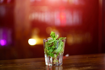 Transparent glass with the leaves of green mint in water on the wooden table. Fresh drink in glass over the blurred background.