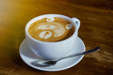 Bear latte art in cappuccino cup on wooden table. Pattern on coffee foam.White cup with coffee on the saucer and spoon. Close-up