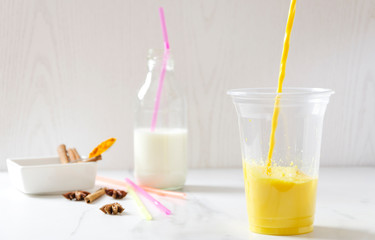 Pouring golden milk into a cup.Tasty turmeric latte with pieces of ice.Fresh and healthy drink for fit lifestyle