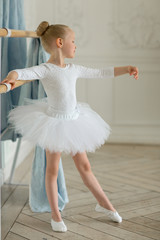 A little girl a ballerina in a white tutu and kitschka is busy at the bench. The concept of children and ballet. Studio © Diana