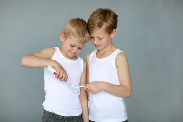 Two brothers brush their teeth against a gray background. The concept of children and oral hygiene