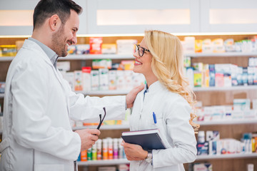 Two smiling healthcare workers looking at each other at modern pharmacy.