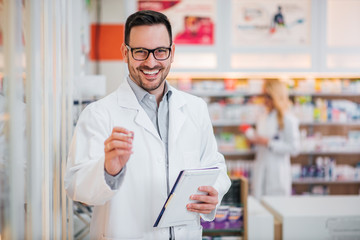 Portrait of a handsome pharmacist with clipboard, smiling at camera.