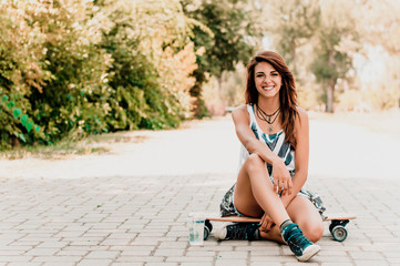 A young stylish girl in short shorts sitting on a skateboard.