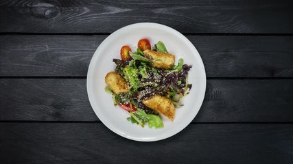 Salad with salmon in breadcrumbs with lettuce and sesame seeds. Rotates on black wooden background. Top view