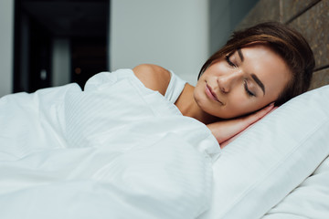 Obraz na płótnie Canvas beautiful brunette woman sleeping on pillow under blanket in bed