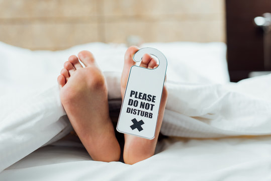 cropped view of woman feet with please do not disturb sign lying in bed