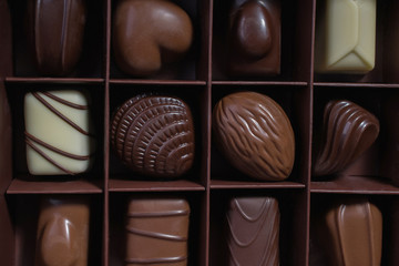 Chocolates in different shapes and colors in gift box on wooden table. Flat lay. Top view