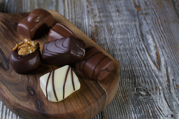 Chocolates in different shapes and colors over rustic wooden board. Atmospheric food photo