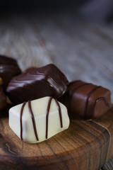 Closeup of Chocolates in different shapes and colors on a chopping board, placed on a dark rustic wooden table.Copy space.