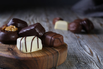 Closeup of Chocolates in different shapes and colors on a chopping board, placed on a dark rustic wooden table.Copy space.