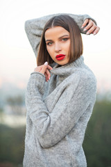 Outdoor portrait of a gorgeous tanned girl wearing knitted sweater posing on a street