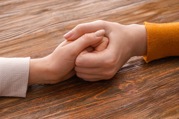 Young women holding hands on wooden background. Concept of support