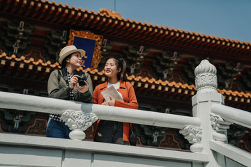 Fototapeta na wymiar Girls photography traveling trip sightseeing concept. low angle view korean women friends travelers standing leaning on white stone railing taking pictures and guide book visit china temple beijing.