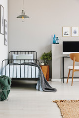Single industrial bed with blue bedding in stylish grey bedroom, copy space on empty wall