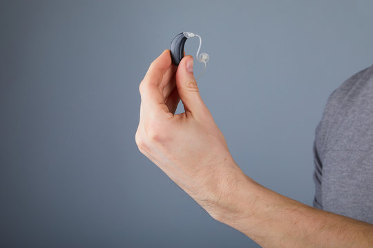 Man holding hearing aid, closeup. Hearing aids on grey background, alternative to surgery. 