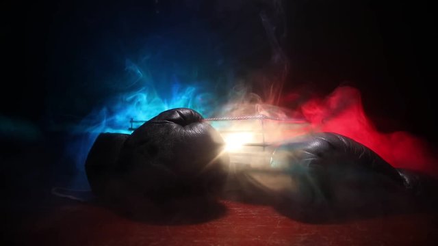 Empty boxing ring with red ropes for match in the stadium arena. Boxing gloves ready to fight. Empty space for text. Foggy background with light. Selective focus