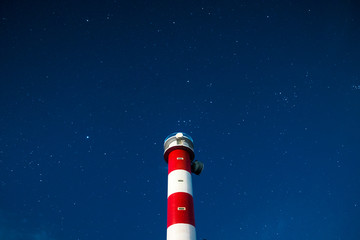 Vertical classic white and red lighthouse during the night with stars and blue sky - travel and destination adventure concept for wonderlust people