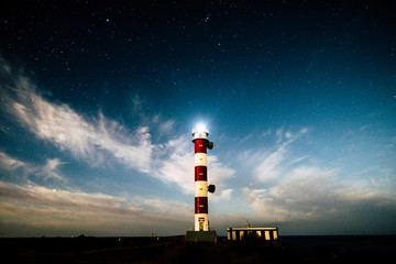 Fototapeta premium Vertical classic white and red lighthouse during the night with stars and blue sky - travel and destination adventure concept for wonderlust people