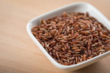 Rotschaliger roher Roter Jasmin Reis in Porzellan Schale auf Holz Hintergrund und ist eine Spezialität aus Kambodscha Asien