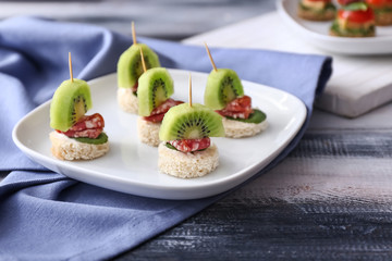 Plate with tasty canapes on wooden table
