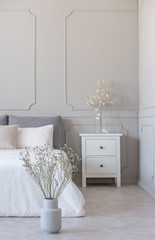 Flowers in grey vase on the floor of simple bedroom with grey wall and white furniture